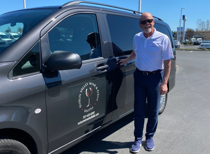 A man standing next to a van with a wine glass on the door.